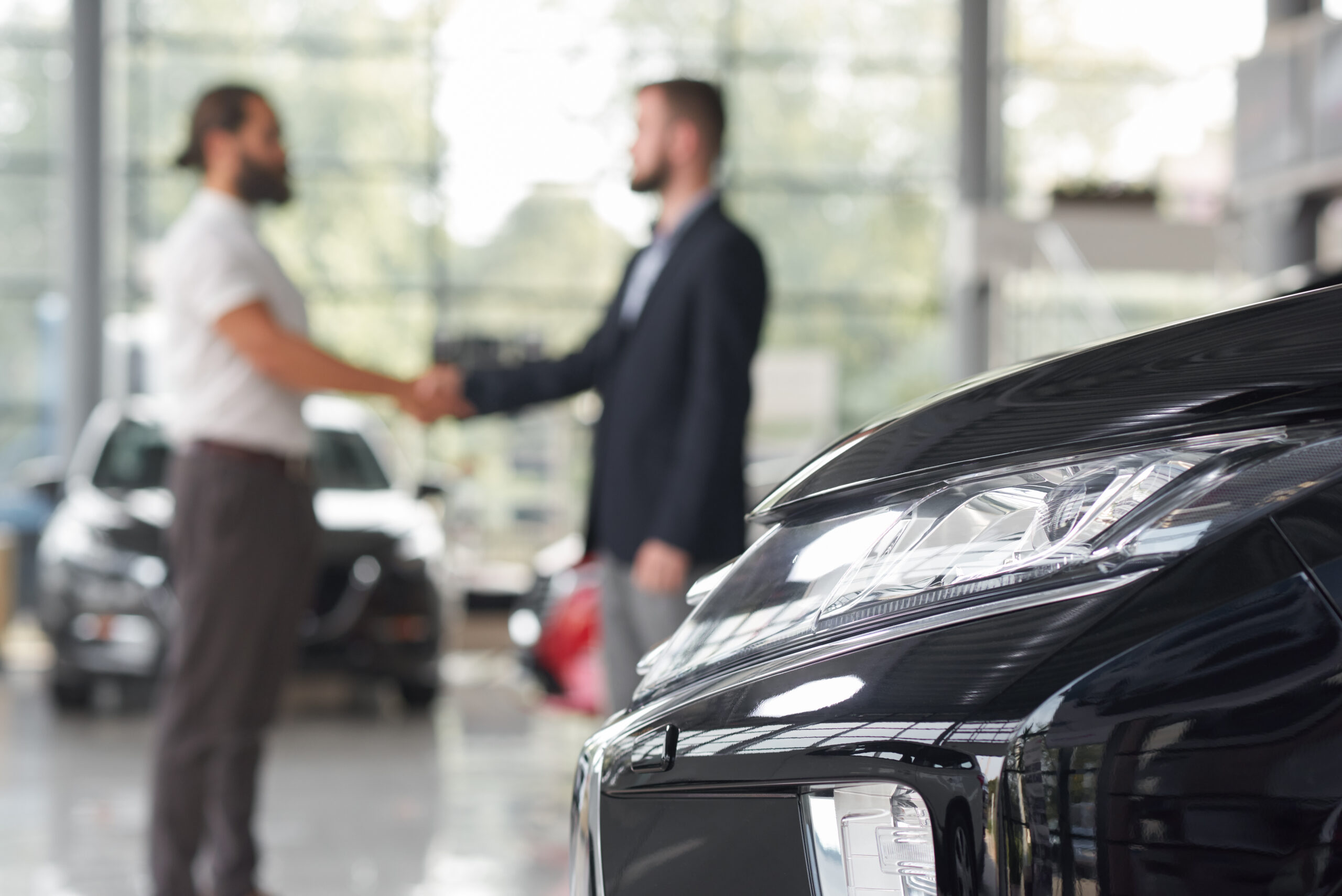Men shaking hands in modern auto showroom. Mechanic working on used vehicle - BENEFITS OF A USED TOYOTA concept image